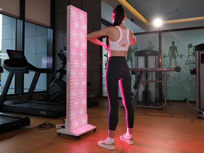 Woman using NovaThera red light therapy LED panel in gym with treadmill and fitness equipment