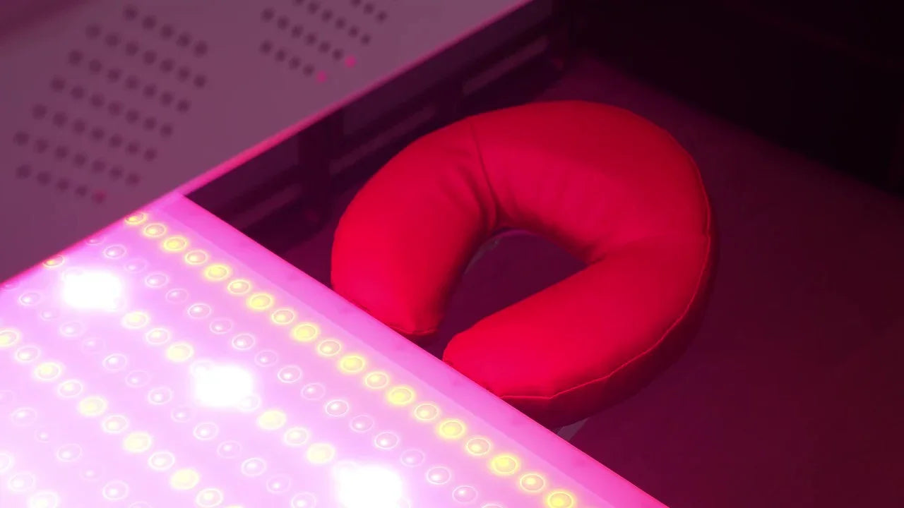 Bright pink LED light panel with red U-shaped neck pillow on dark surface in dim room