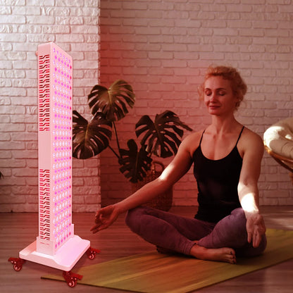 Woman meditating with eyes closed near a pink LED light therapy panel in a cozy room with plants