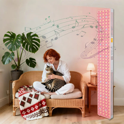 Woman in pajamas sitting on wicker sofa with cat, next to pink light therapy panel in cozy living room